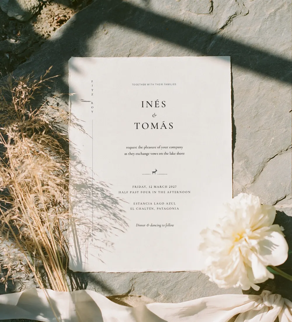 Glacier wedding invitation on handmade paper on grey slate with dried grasses, a white peony and silk ribbon