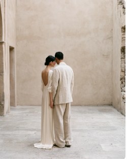 Couple in cream linen standing together against a plaster wall