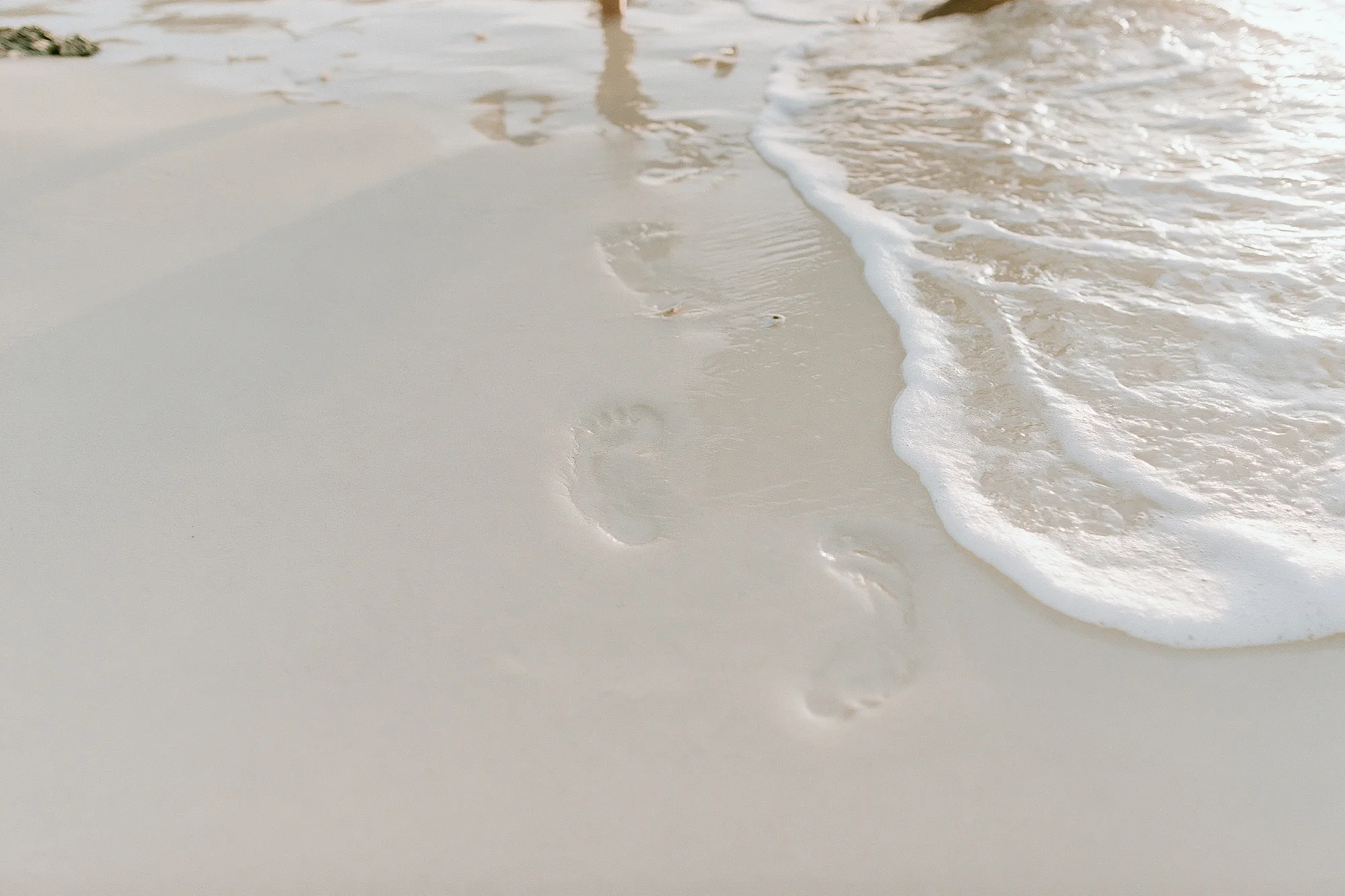 Footprints on white sand at the shoreline