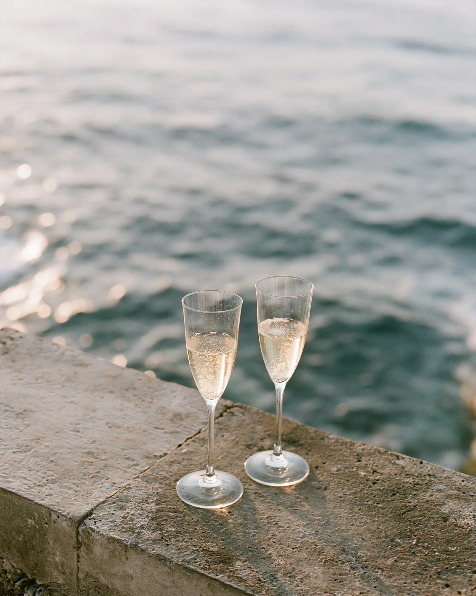 Two champagne glasses on a stone ledge above the sea