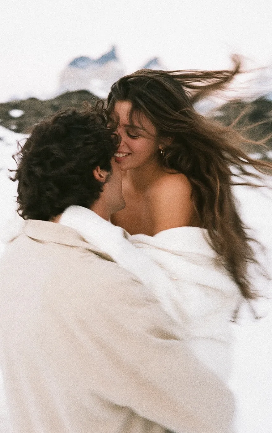 Couple embracing and laughing, wrapped in a white blanket in the wind