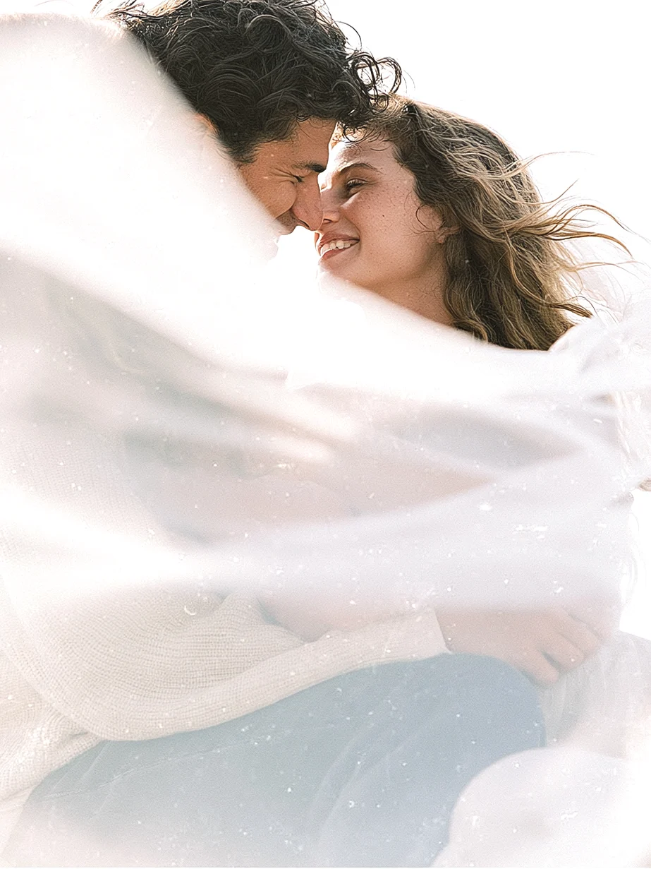 Couple laughing together, wrapped in a white veil blowing in the wind