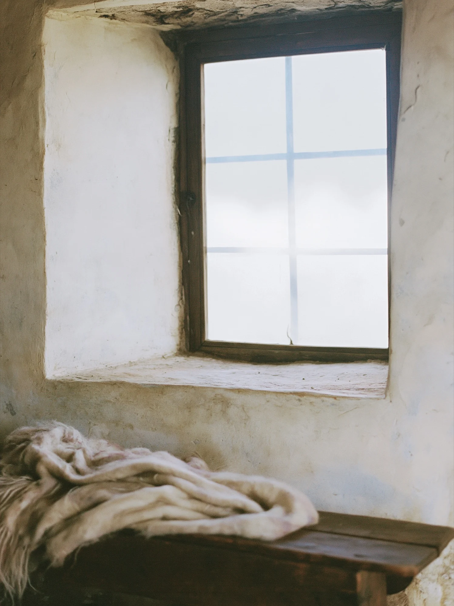 Stone-walled room with a deep window and a draped linen throw