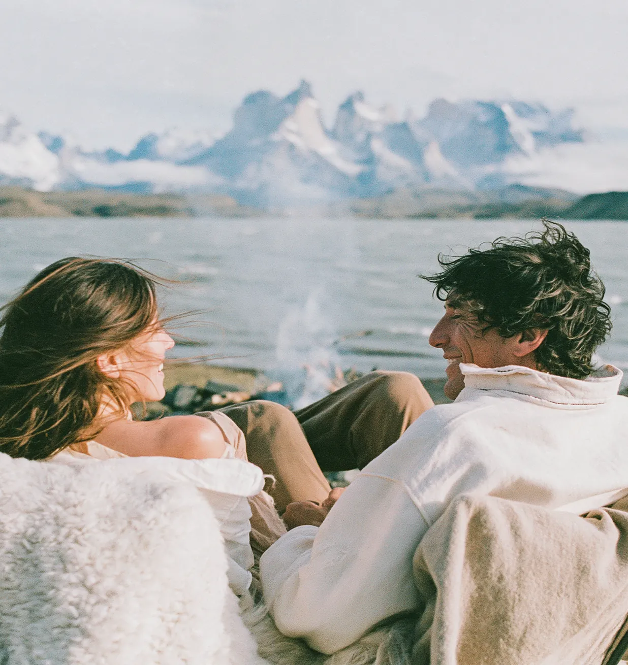 Couple sitting on a lakeshore with snow-capped mountains behind