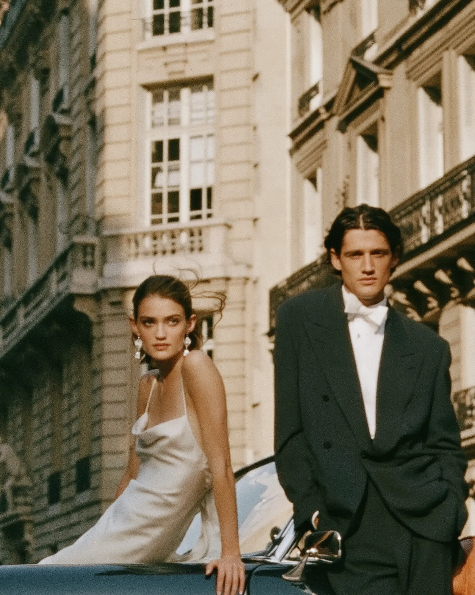 Couple in evening wear leaning on a classic car in Paris