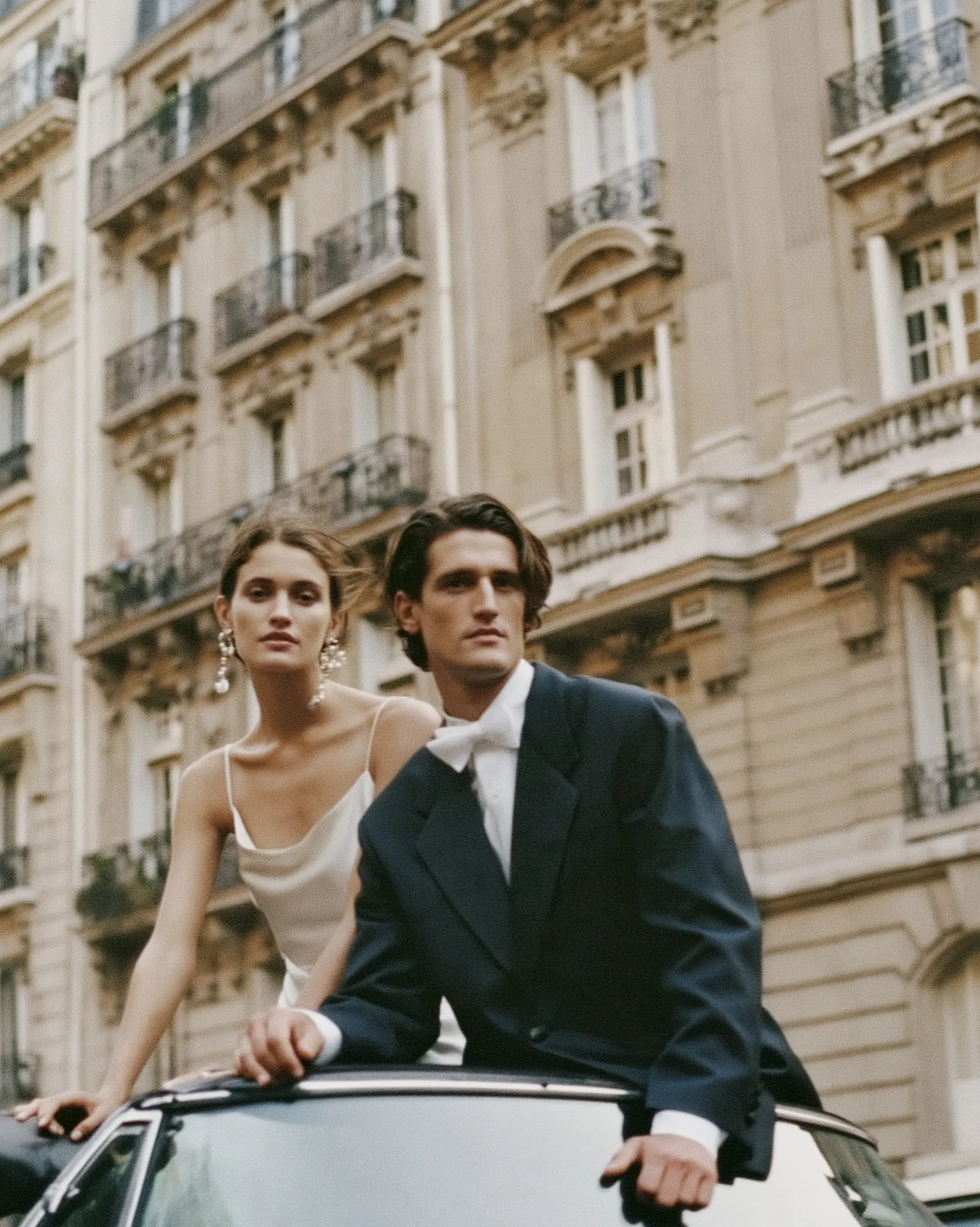 Bride and groom in black tie standing in a vintage convertible on a Paris street