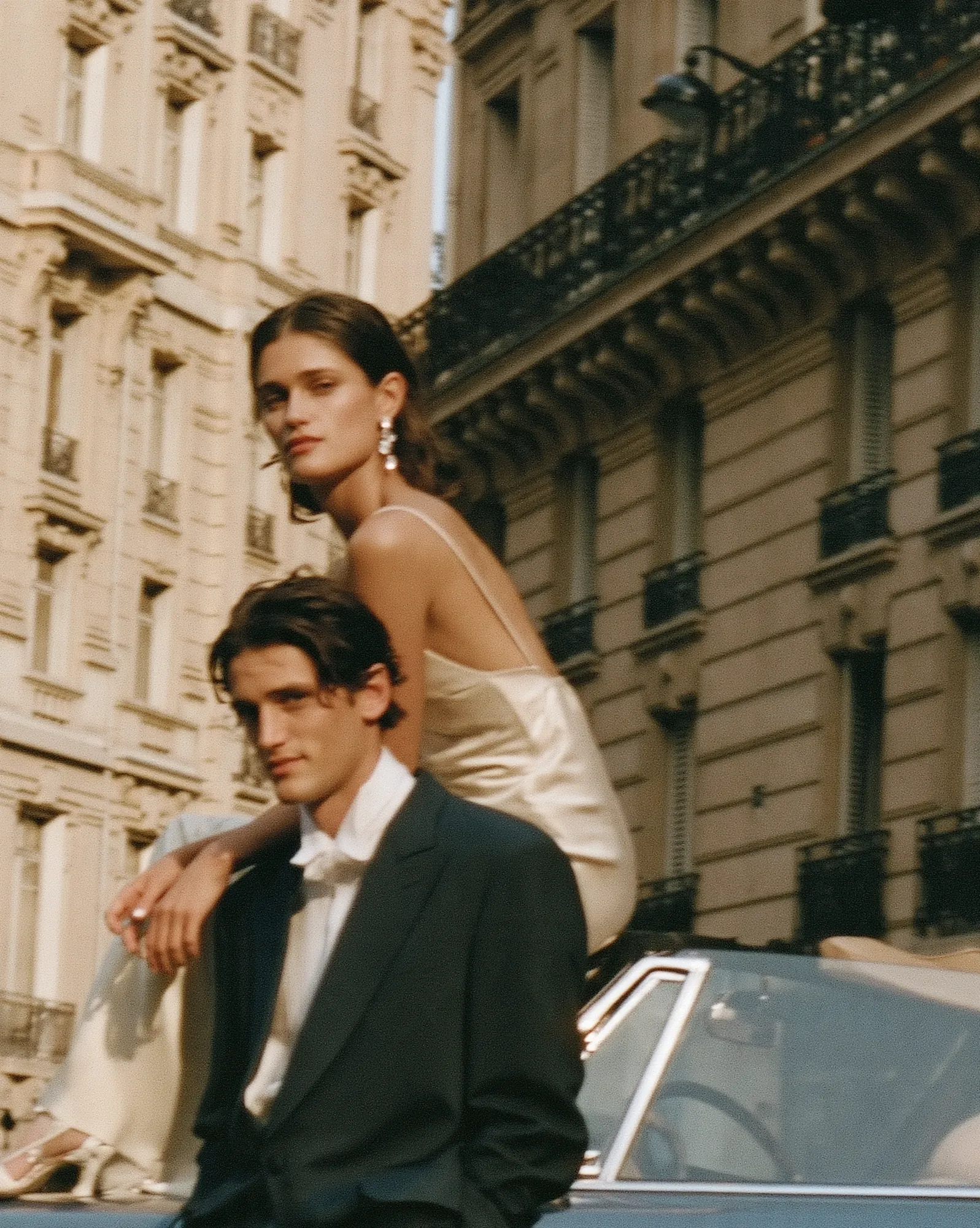 Couple beside a classic car below Parisian balconies