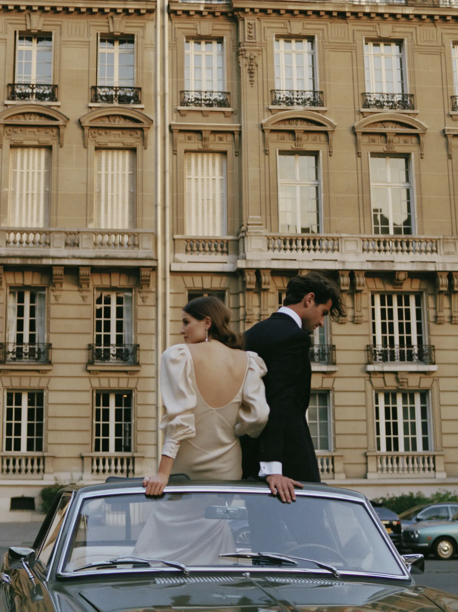 Bride and groom standing in a convertible on a Paris street