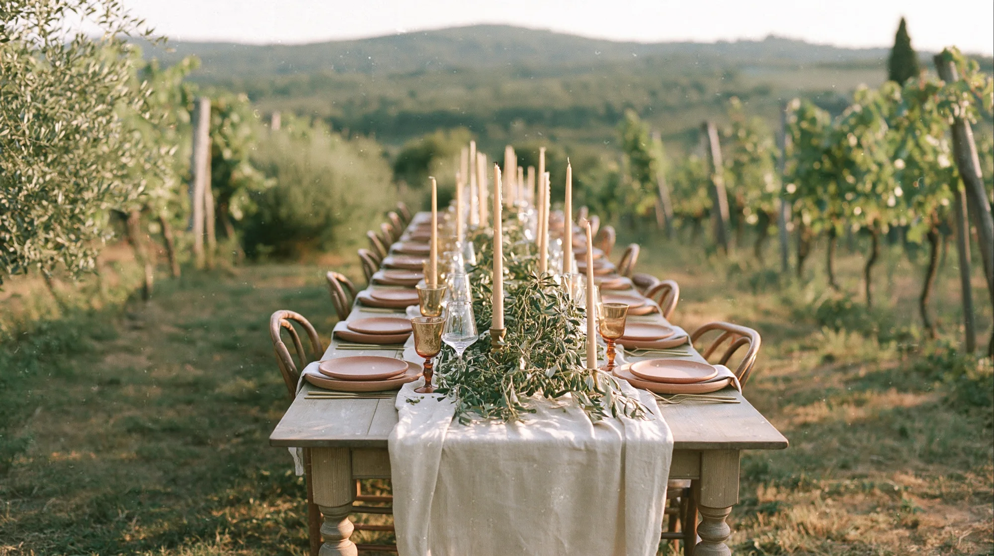 Long wedding table with candles set in a Tuscan vineyard at sunset