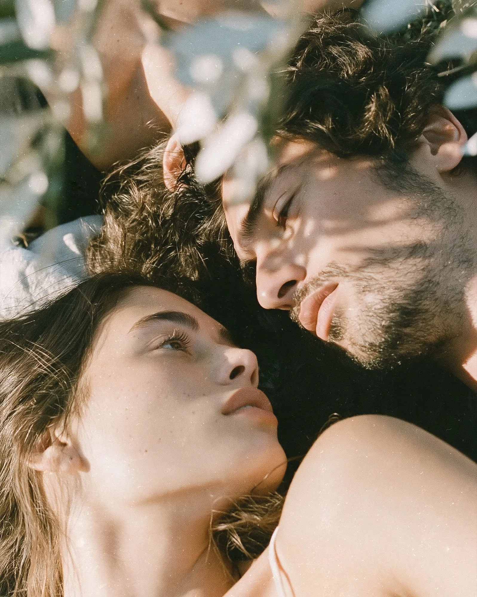 Couple lying close together among olive leaves in soft sunlight