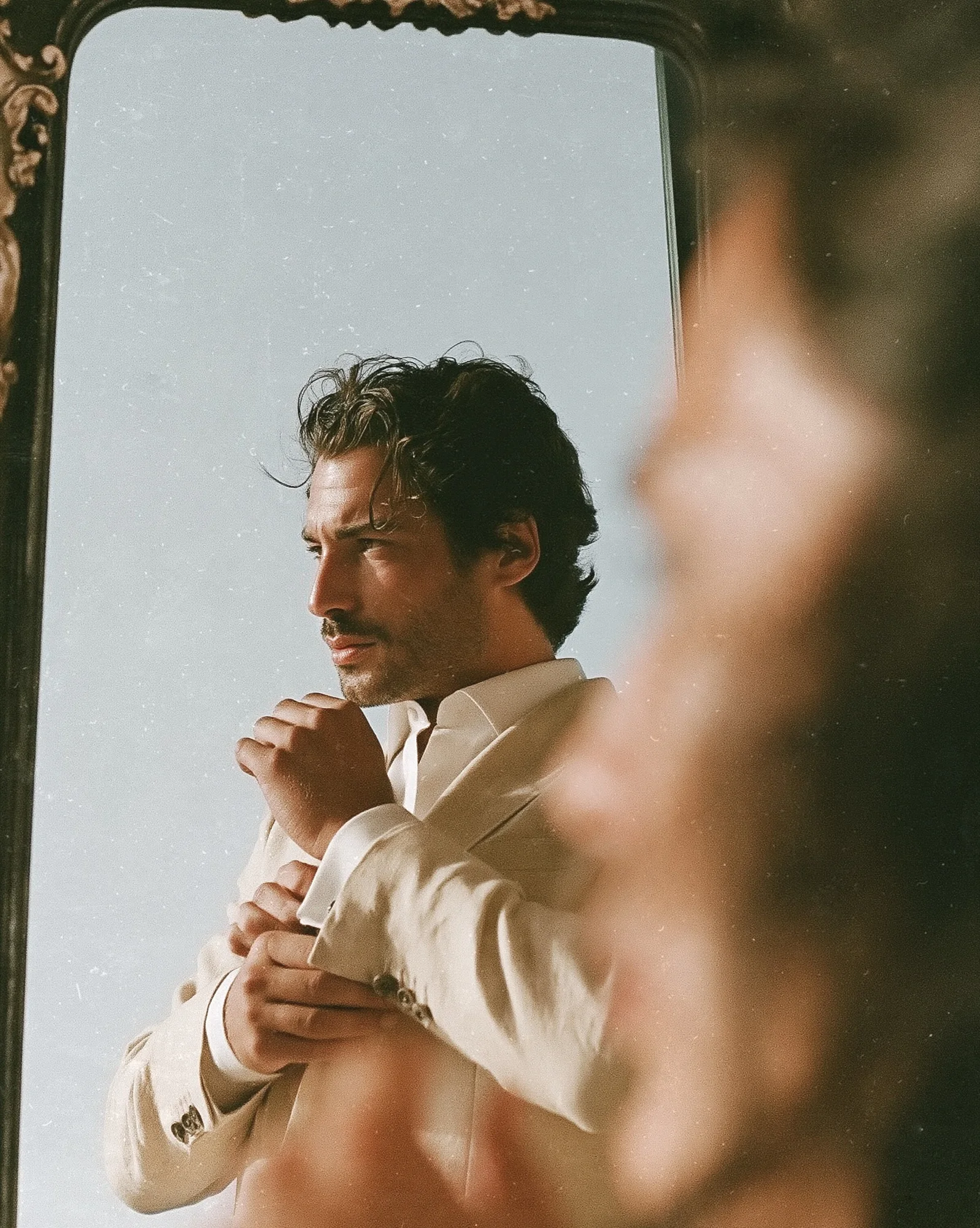 Groom in a linen suit reflected in a mirror while getting ready